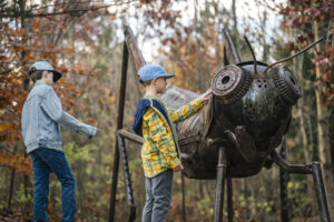 Boys discovering giant metal grasshopper on Centennial Pathway
