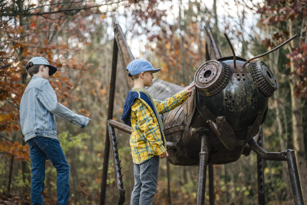 Boys discovering giant metal grasshopper on Centennial Pathway
